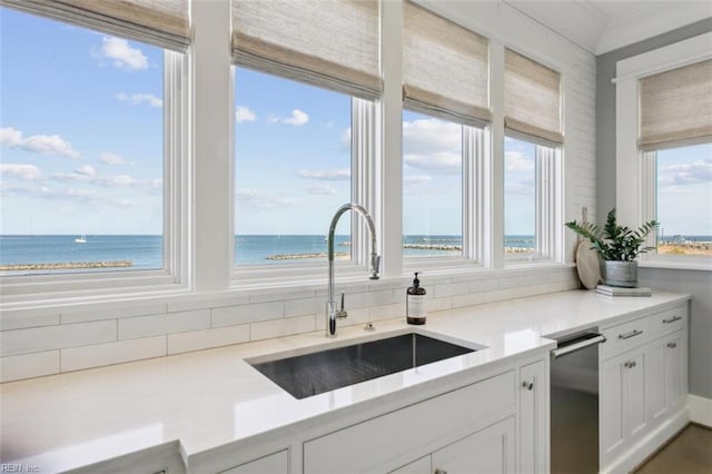 kitchen featuring stainless steel dishwasher, sink, a view of the beach, a water view, and white cabinets