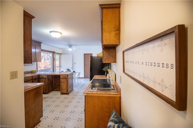 kitchen featuring black refrigerator, kitchen peninsula, ceiling fan, and stainless steel gas stovetop