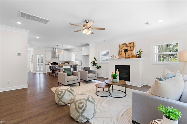 living room featuring dark hardwood / wood-style floors, plenty of natural light, crown molding, and ceiling fan