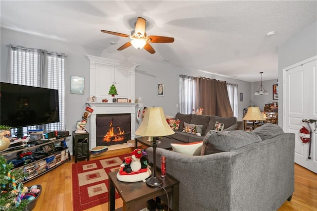 living room with ceiling fan with notable chandelier, light wood-type flooring, and a textured ceiling