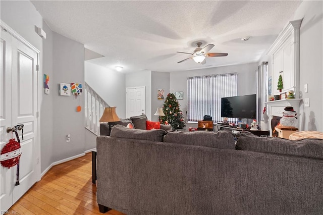 living room with a fireplace, a textured ceiling, light wood-type flooring, and ceiling fan