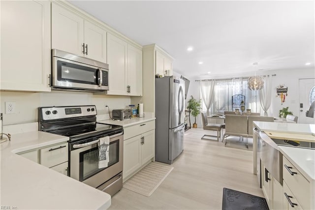 kitchen with light hardwood / wood-style floors, decorative light fixtures, and appliances with stainless steel finishes