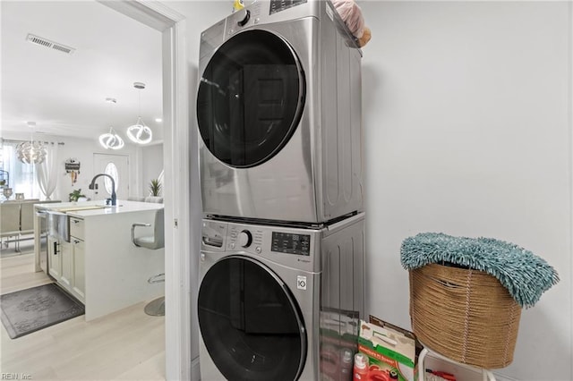 washroom featuring sink, light hardwood / wood-style floors, stacked washer and clothes dryer, and an inviting chandelier