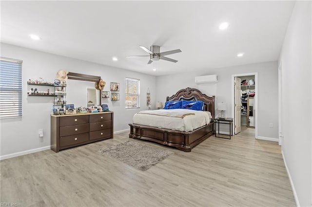 bedroom with light wood-type flooring, a wall mounted AC, ceiling fan, a spacious closet, and a closet