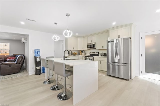 kitchen featuring a breakfast bar, sink, light hardwood / wood-style flooring, appliances with stainless steel finishes, and decorative light fixtures