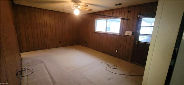 unfurnished room with light carpet, ceiling fan, and wood walls