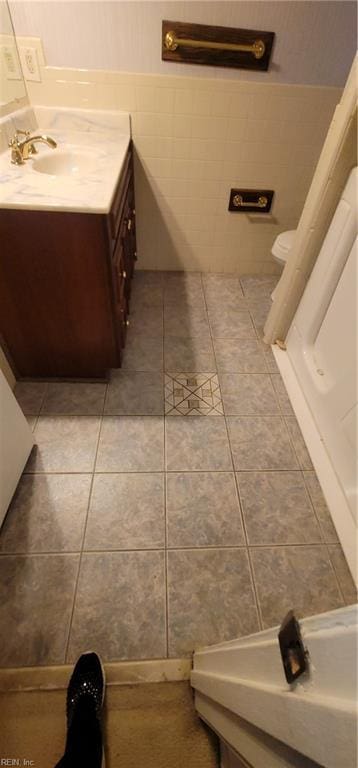 bathroom featuring toilet, tile patterned floors, tile walls, and vanity