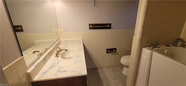 bathroom with toilet, tile patterned flooring, tile walls, and vanity