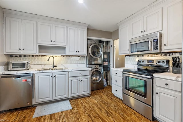 kitchen featuring sink, stacked washing maching and dryer, dark hardwood / wood-style flooring, white cabinets, and appliances with stainless steel finishes