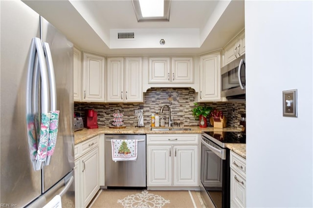 kitchen with sink, stainless steel appliances, light stone counters, and a tray ceiling