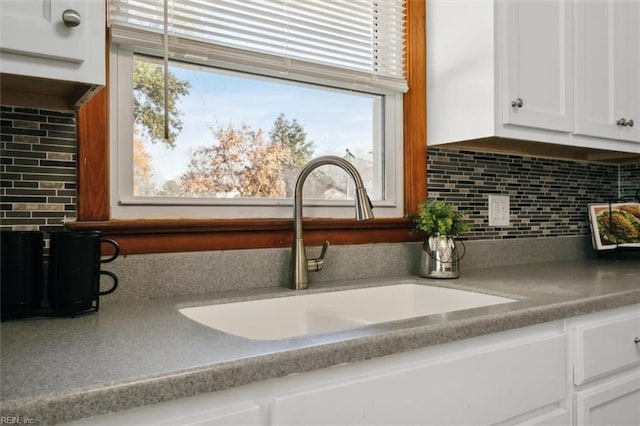 interior details featuring decorative backsplash, white cabinetry, and sink