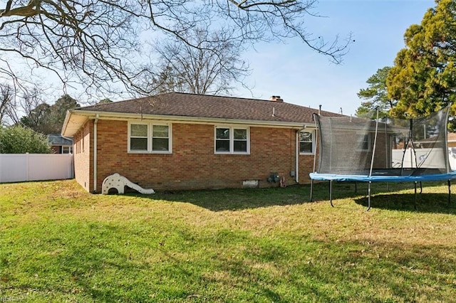 back of property featuring a trampoline and a lawn