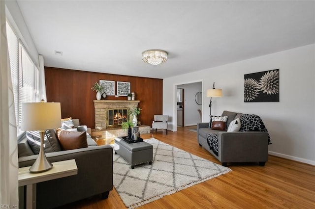 living room featuring hardwood / wood-style floors, an inviting chandelier, a brick fireplace, and wood walls