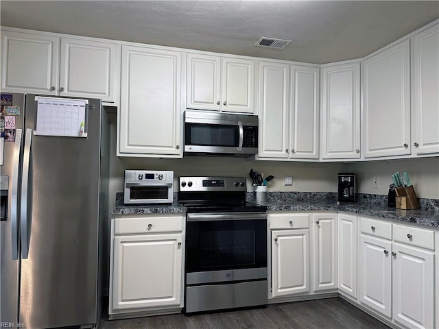 kitchen featuring white cabinets, dark stone countertops, dark wood-type flooring, and appliances with stainless steel finishes