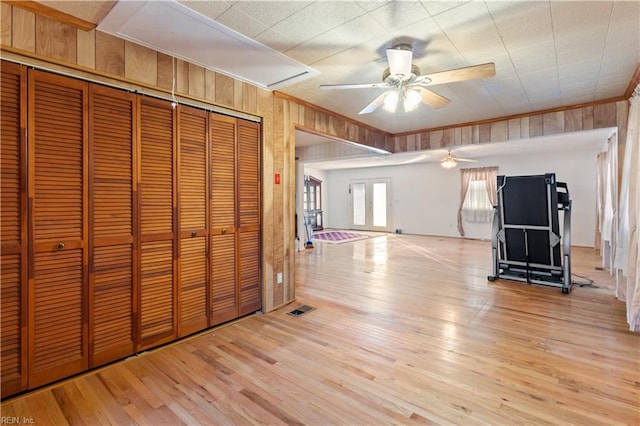 unfurnished bedroom with light wood-type flooring, ornamental molding, ceiling fan, wooden walls, and a closet