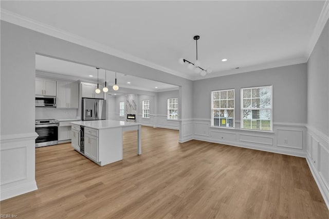 kitchen with appliances with stainless steel finishes, crown molding, white cabinetry, and decorative light fixtures