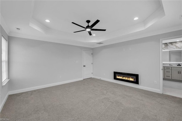 unfurnished living room featuring ceiling fan, light colored carpet, a tray ceiling, and ornamental molding