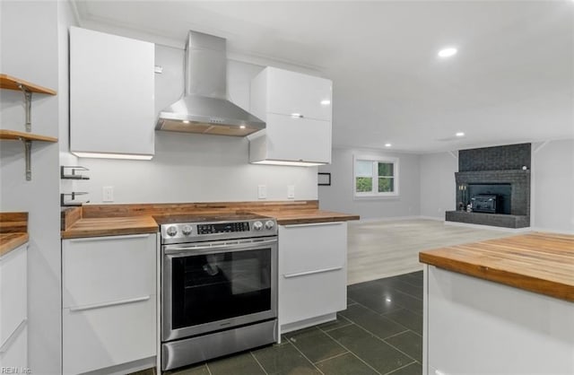 kitchen featuring butcher block countertops, white cabinetry, electric range, and wall chimney range hood