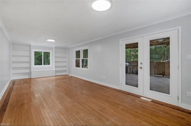 spare room featuring built in shelves, crown molding, light hardwood / wood-style flooring, and french doors