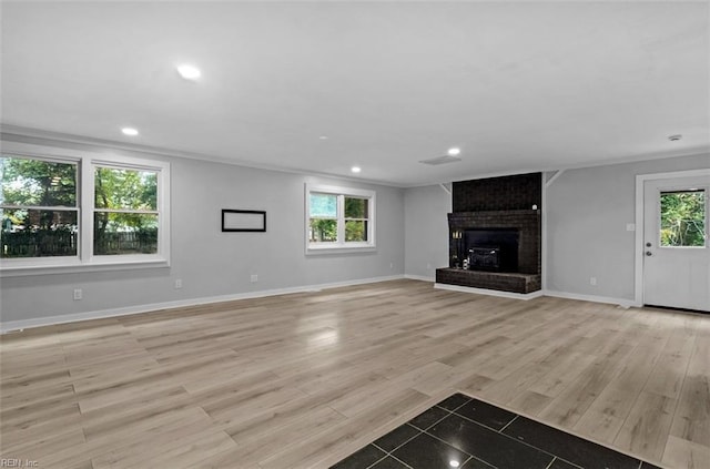 unfurnished living room featuring plenty of natural light, light hardwood / wood-style floors, crown molding, and a fireplace