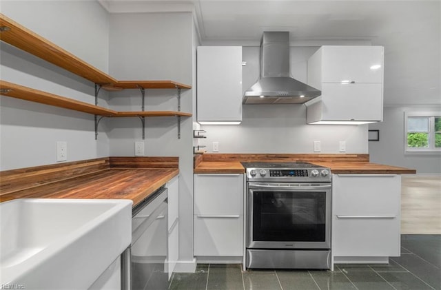 kitchen featuring butcher block counters, wall chimney range hood, sink, appliances with stainless steel finishes, and white cabinetry