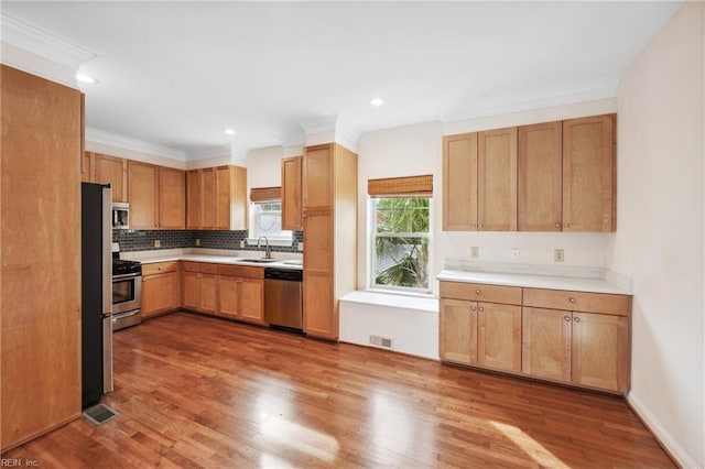 kitchen with appliances with stainless steel finishes, backsplash, crown molding, sink, and hardwood / wood-style floors