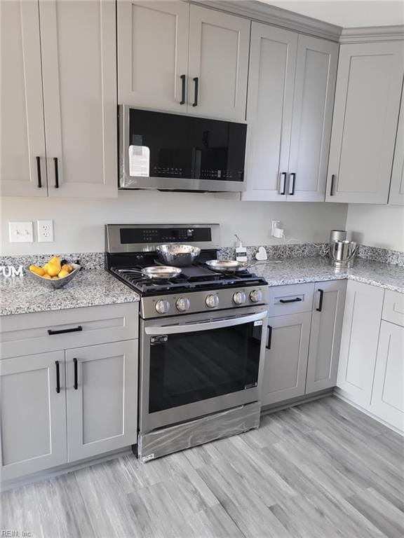 kitchen featuring gray cabinets, stainless steel appliances, light stone counters, and light hardwood / wood-style floors