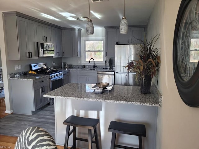 kitchen with pendant lighting, a breakfast bar, dark hardwood / wood-style floors, gray cabinets, and stainless steel appliances