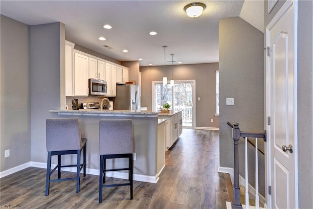 kitchen featuring white cabinetry, dark wood-type flooring, pendant lighting, a breakfast bar area, and appliances with stainless steel finishes