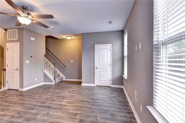 unfurnished room with a healthy amount of sunlight, ceiling fan, dark wood-type flooring, and a textured ceiling