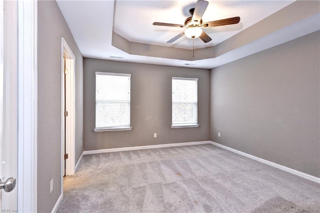 carpeted spare room featuring a raised ceiling and ceiling fan