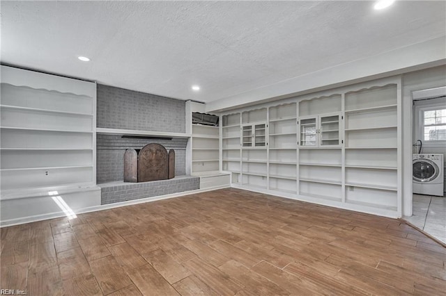 unfurnished living room with hardwood / wood-style flooring, a fireplace, washer / dryer, and a textured ceiling