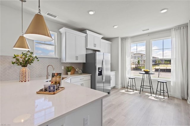 kitchen featuring decorative backsplash, stainless steel fridge with ice dispenser, white cabinets, and pendant lighting