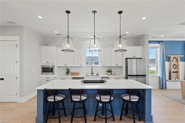 kitchen with appliances with stainless steel finishes, backsplash, light hardwood / wood-style floors, white cabinetry, and a large island