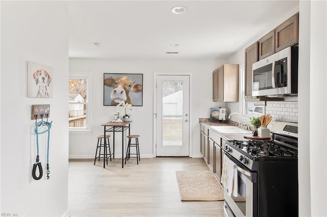 kitchen featuring backsplash, sink, light hardwood / wood-style flooring, and appliances with stainless steel finishes