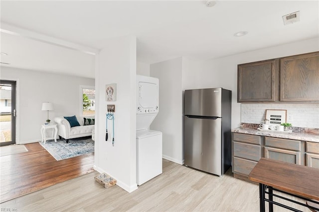 kitchen featuring decorative backsplash, light wood-type flooring, stacked washing maching and dryer, and stainless steel refrigerator