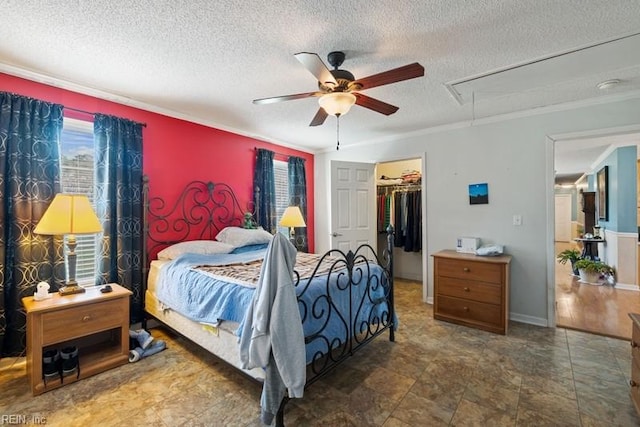 bedroom featuring ceiling fan, a textured ceiling, a walk in closet, a closet, and ornamental molding