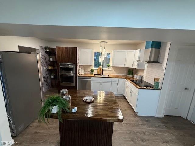 kitchen with white cabinetry, sink, wall chimney range hood, a kitchen island, and appliances with stainless steel finishes