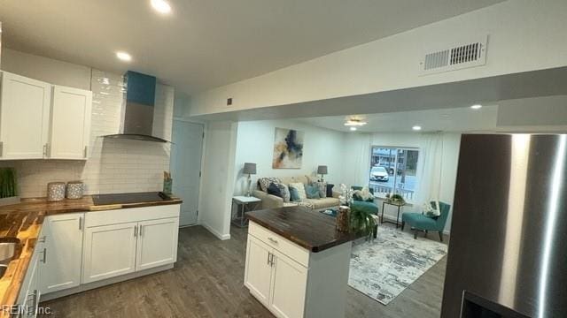 kitchen with black electric cooktop, wall chimney range hood, dark hardwood / wood-style floors, white cabinetry, and butcher block counters