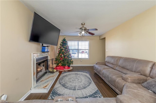 living room featuring ceiling fan, a premium fireplace, and dark wood-type flooring