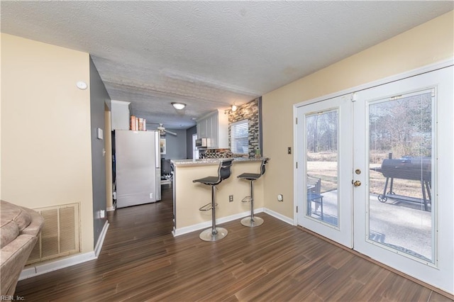 kitchen with french doors, kitchen peninsula, white fridge, a kitchen bar, and white cabinets