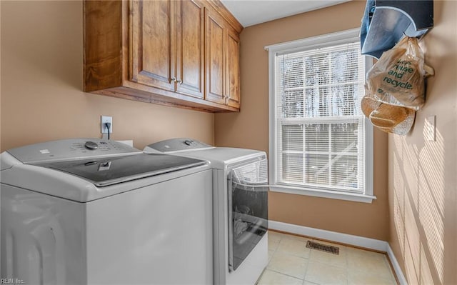 laundry area featuring washer and dryer, cabinets, light tile patterned floors, and a wealth of natural light