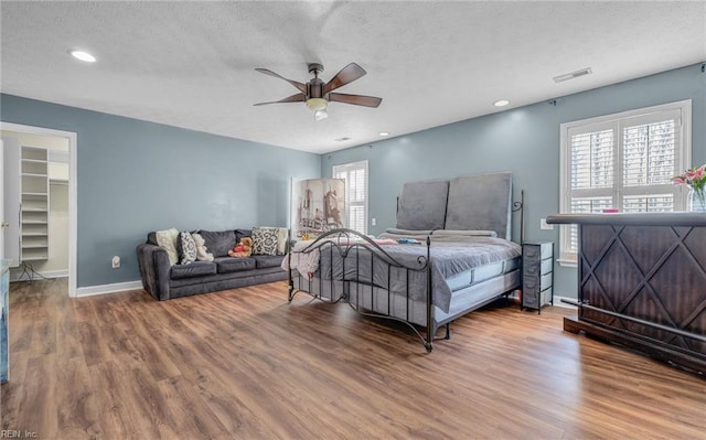 bedroom with hardwood / wood-style floors, a walk in closet, a textured ceiling, and ceiling fan