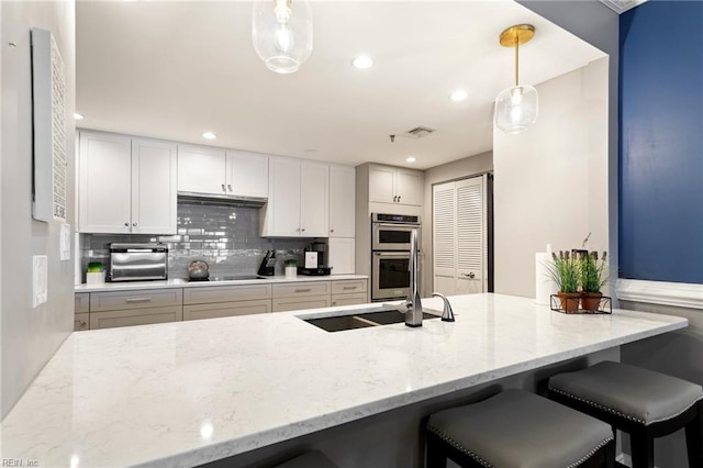 kitchen with white cabinetry, light stone counters, double oven, pendant lighting, and decorative backsplash