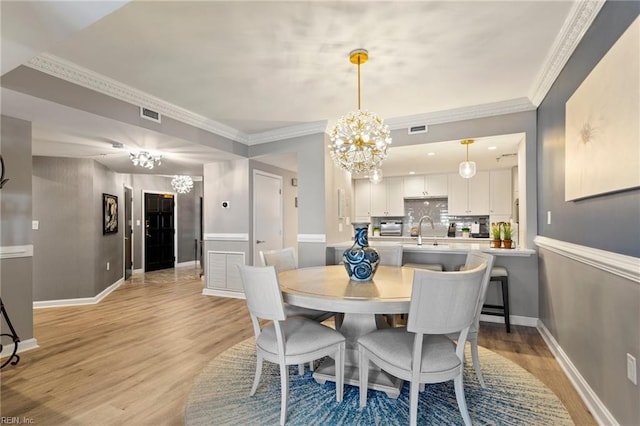 dining area featuring light hardwood / wood-style floors, an inviting chandelier, crown molding, and sink