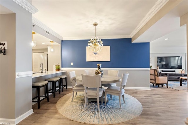 dining area featuring hardwood / wood-style floors, an inviting chandelier, ornamental molding, and sink