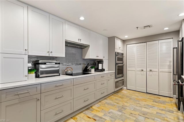 kitchen with tasteful backsplash, black electric stovetop, stainless steel double oven, and light hardwood / wood-style flooring