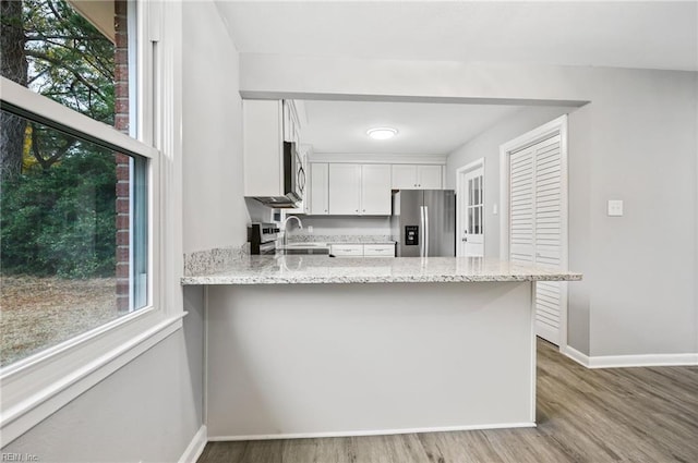 kitchen with light stone countertops, kitchen peninsula, light hardwood / wood-style floors, white cabinets, and appliances with stainless steel finishes