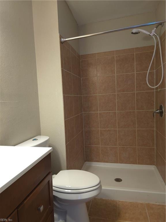 bathroom with tile patterned flooring, vanity, toilet, and a tile shower