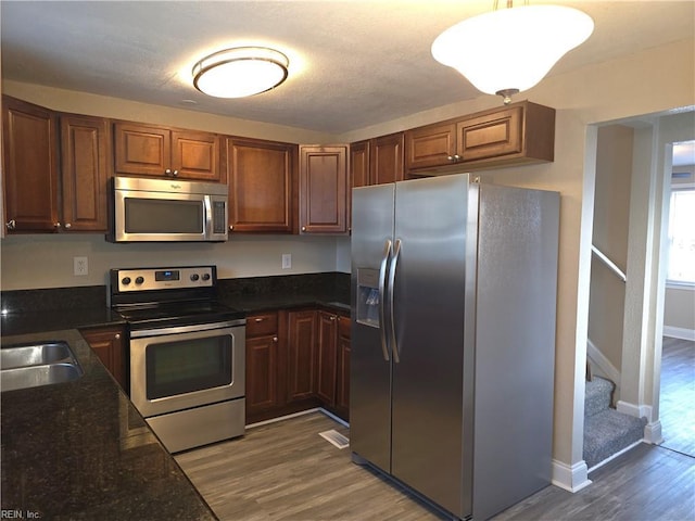 kitchen featuring dark stone countertops, dark hardwood / wood-style flooring, stainless steel appliances, and sink